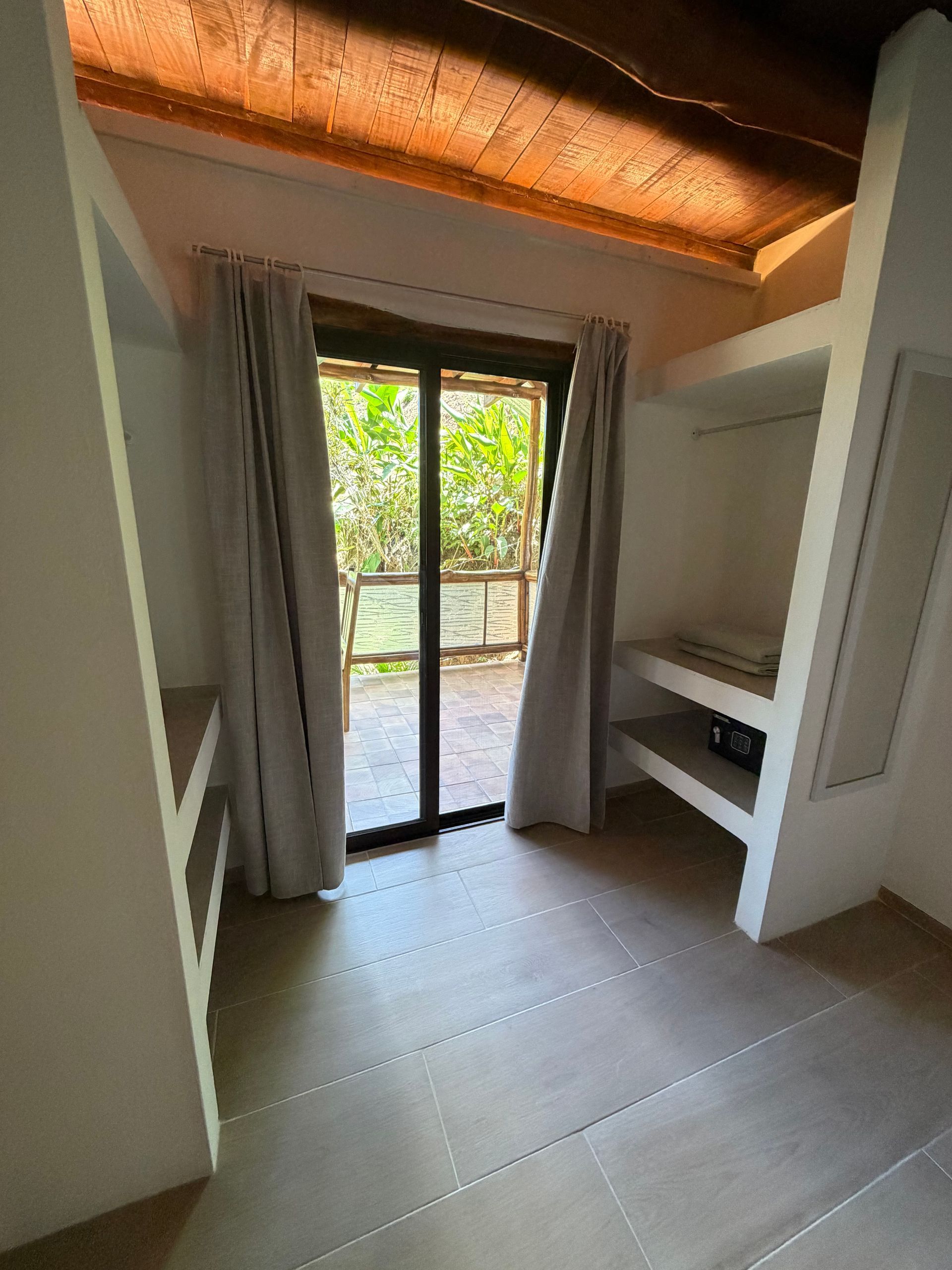 Small bedroom with open sliding door to a balcony, white built-in shelves, and curtains.