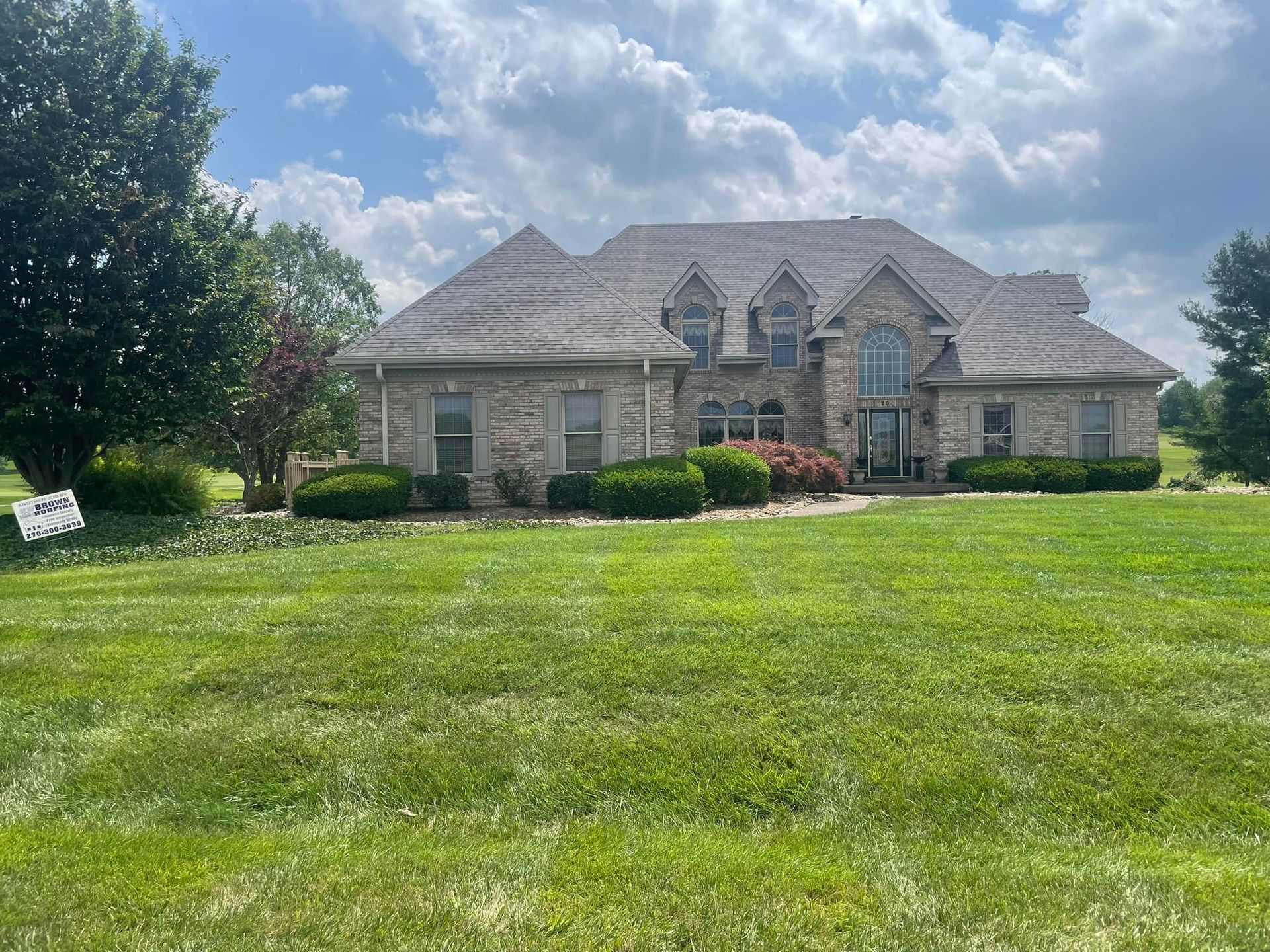 Large brick house with brown roof and green lawn on a sunny day.