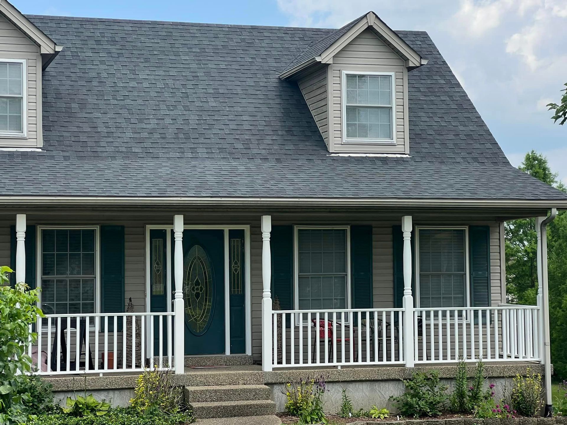 Two-story house with gray roof, white porch, and green shutters.