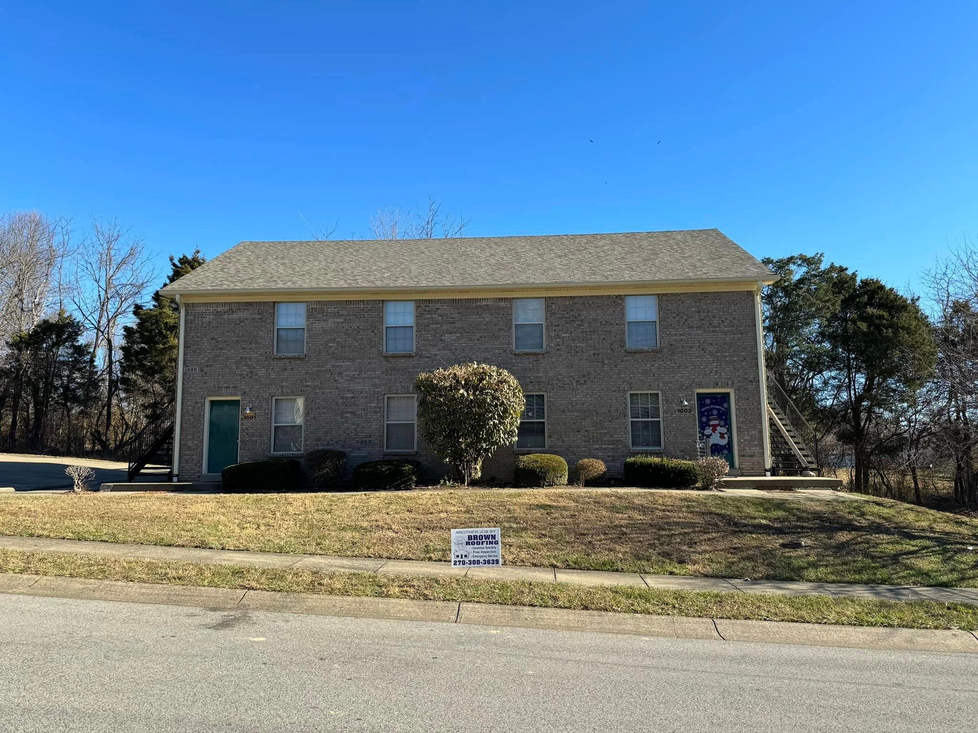 Two-story brick building with multiple units; green and blue doors, clear blue sky.
