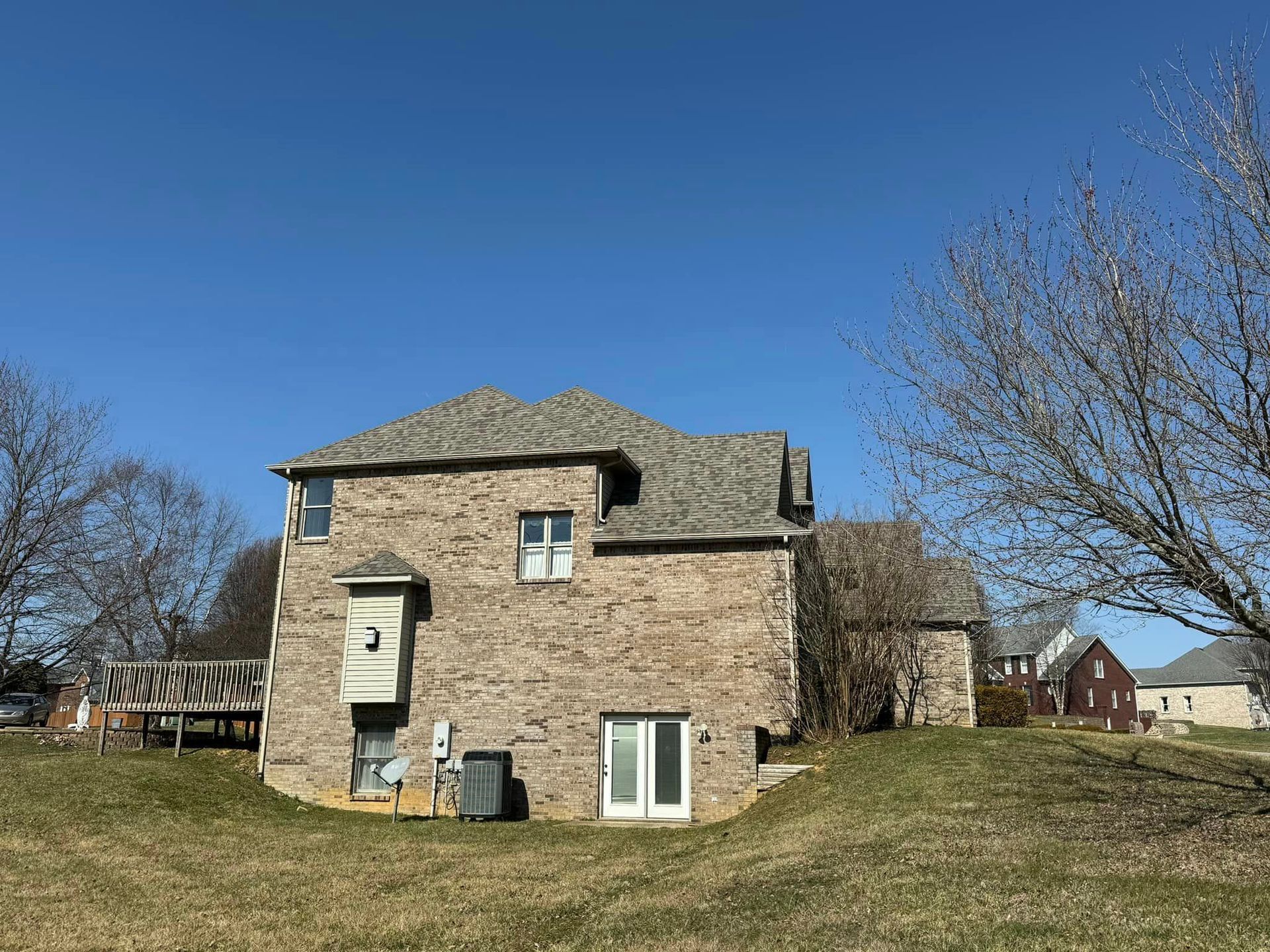 Brick house with a gray roof and a blue sky. There is a grassy hill in front of the house.