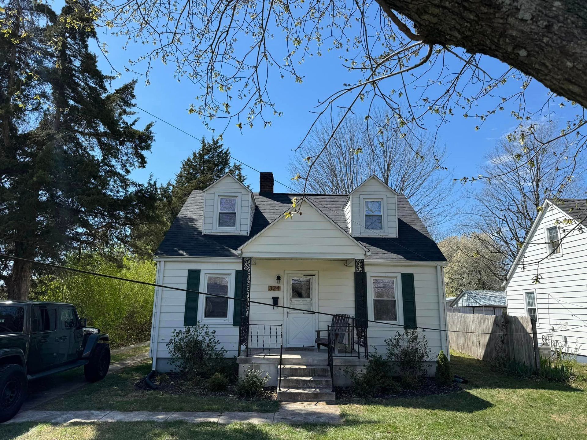 Small white house with dark roof and two dormers, steps leading to porch, blue sky.