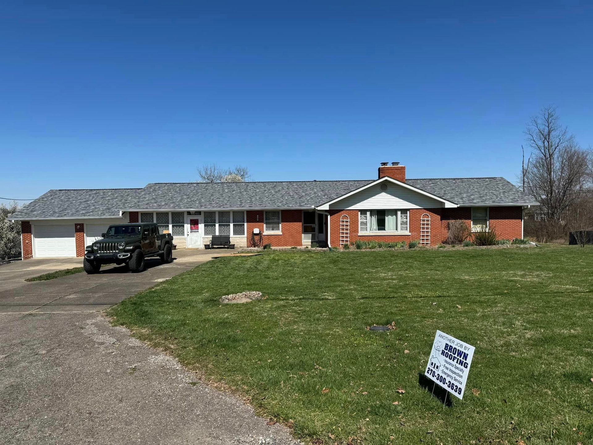 Ranch-style brick house with a newly installed gray roof; a black Jeep in the driveway. A blue sky is visible.