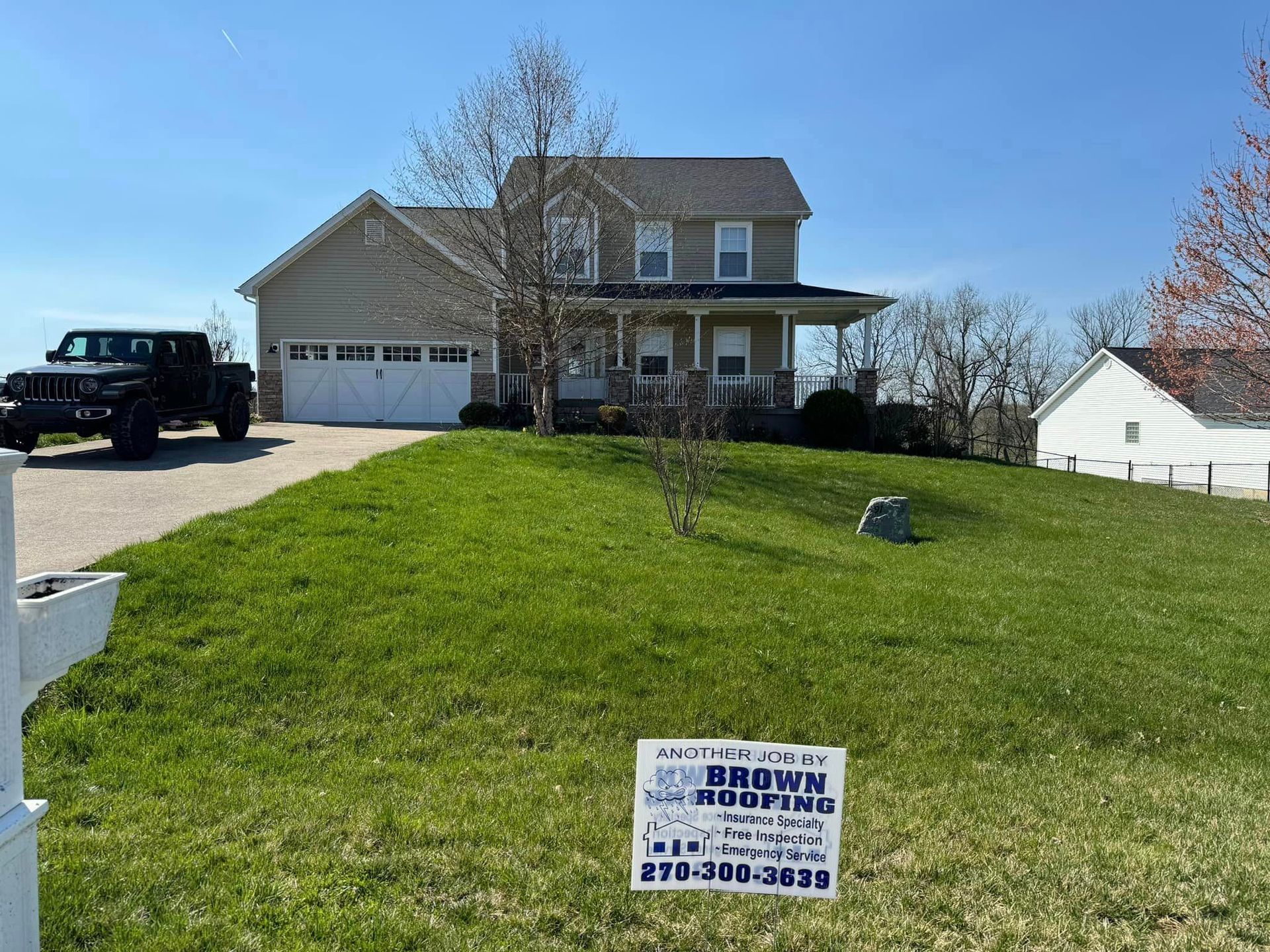 House with a lawn and driveway, a black truck, and a Brown Roofing sign on the grass.