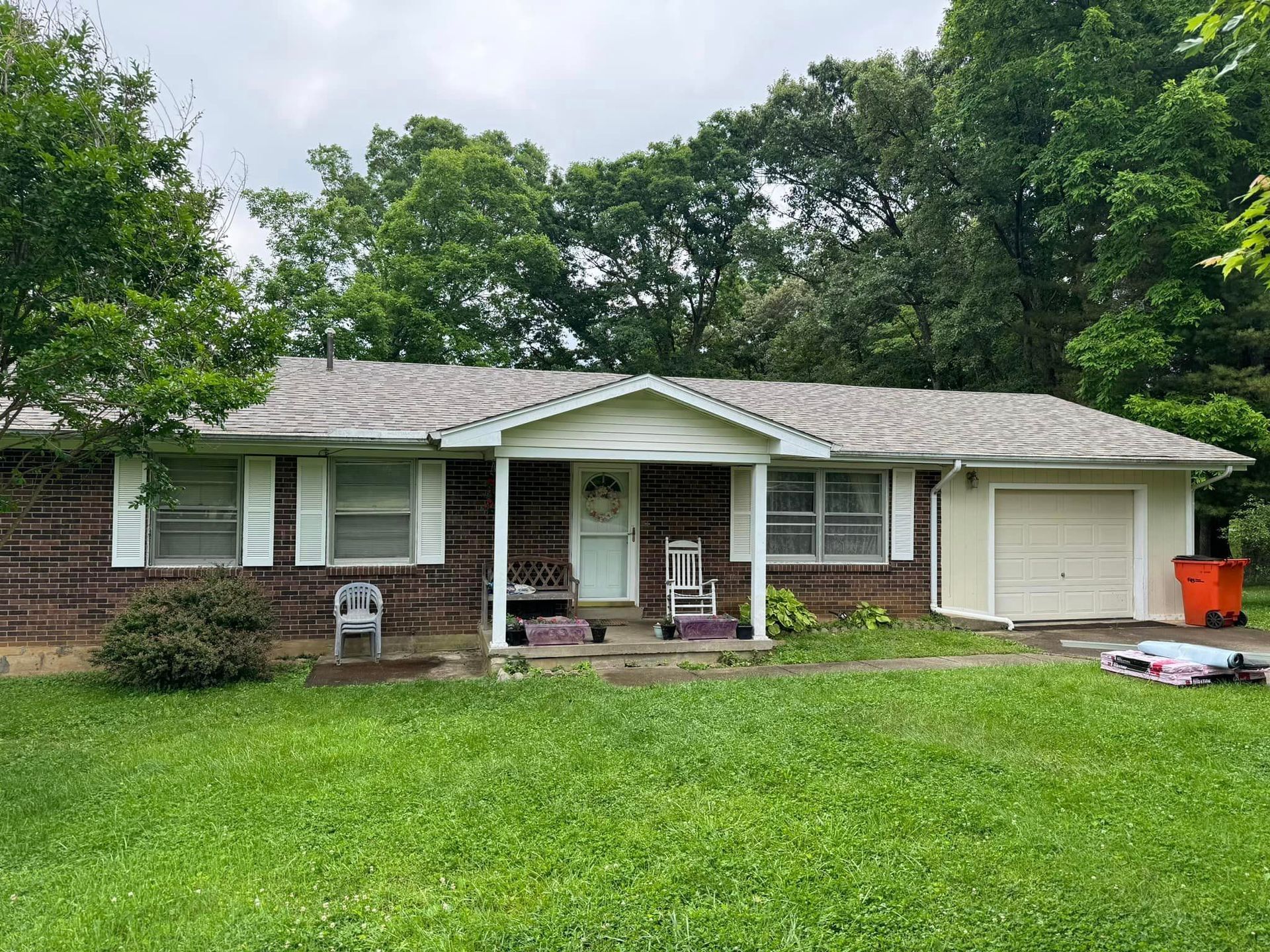 Ranch-style house with brick siding, a small porch, and attached garage on a green lawn with trees in the background.