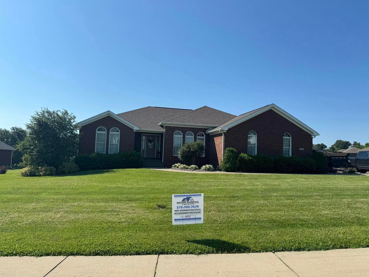 Brick house with a green lawn and blue sky. A sign is placed in the yard.