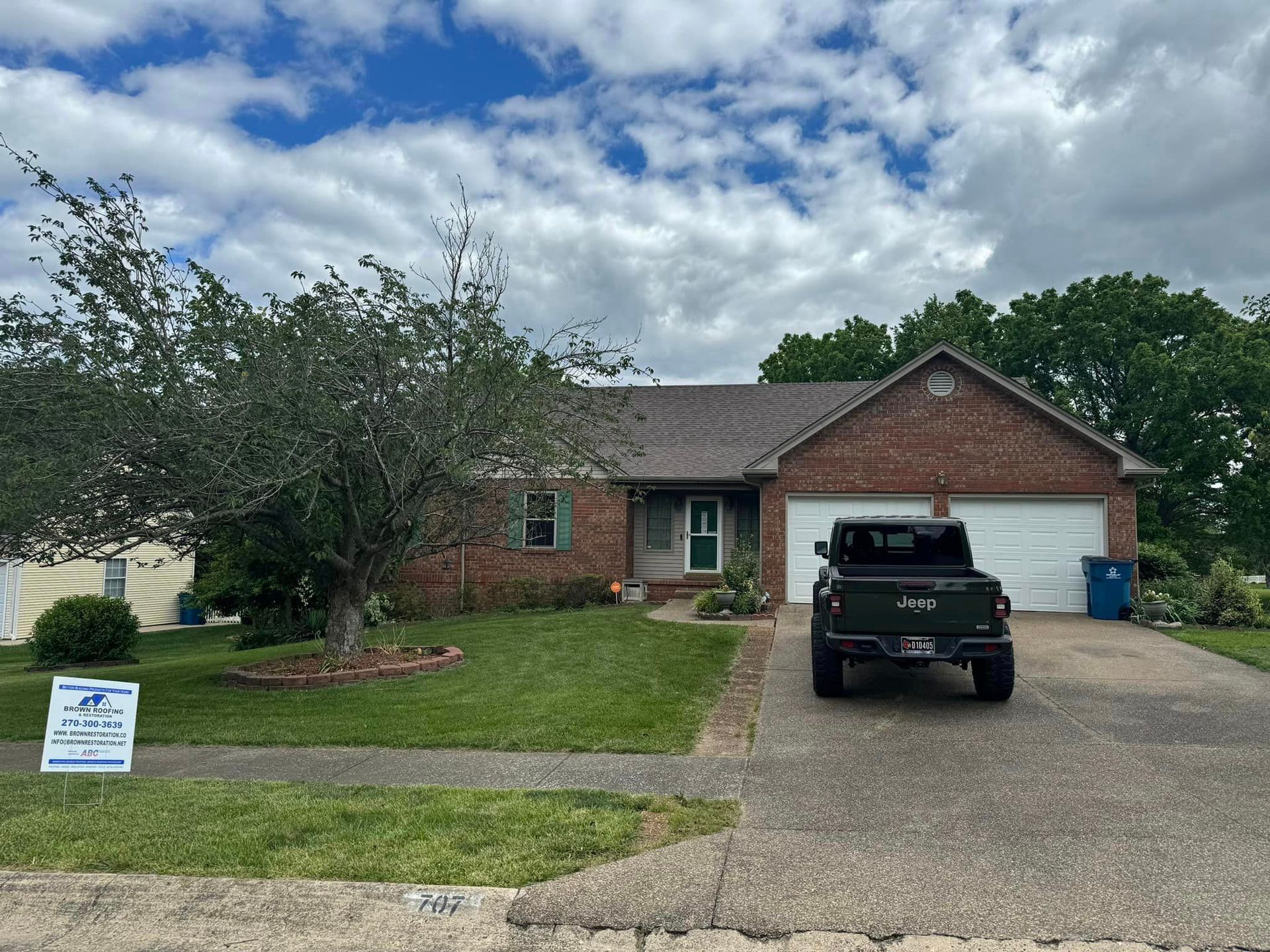 Brick house with green lawn, a dark truck parked in front of the garage. Cloudy sky.