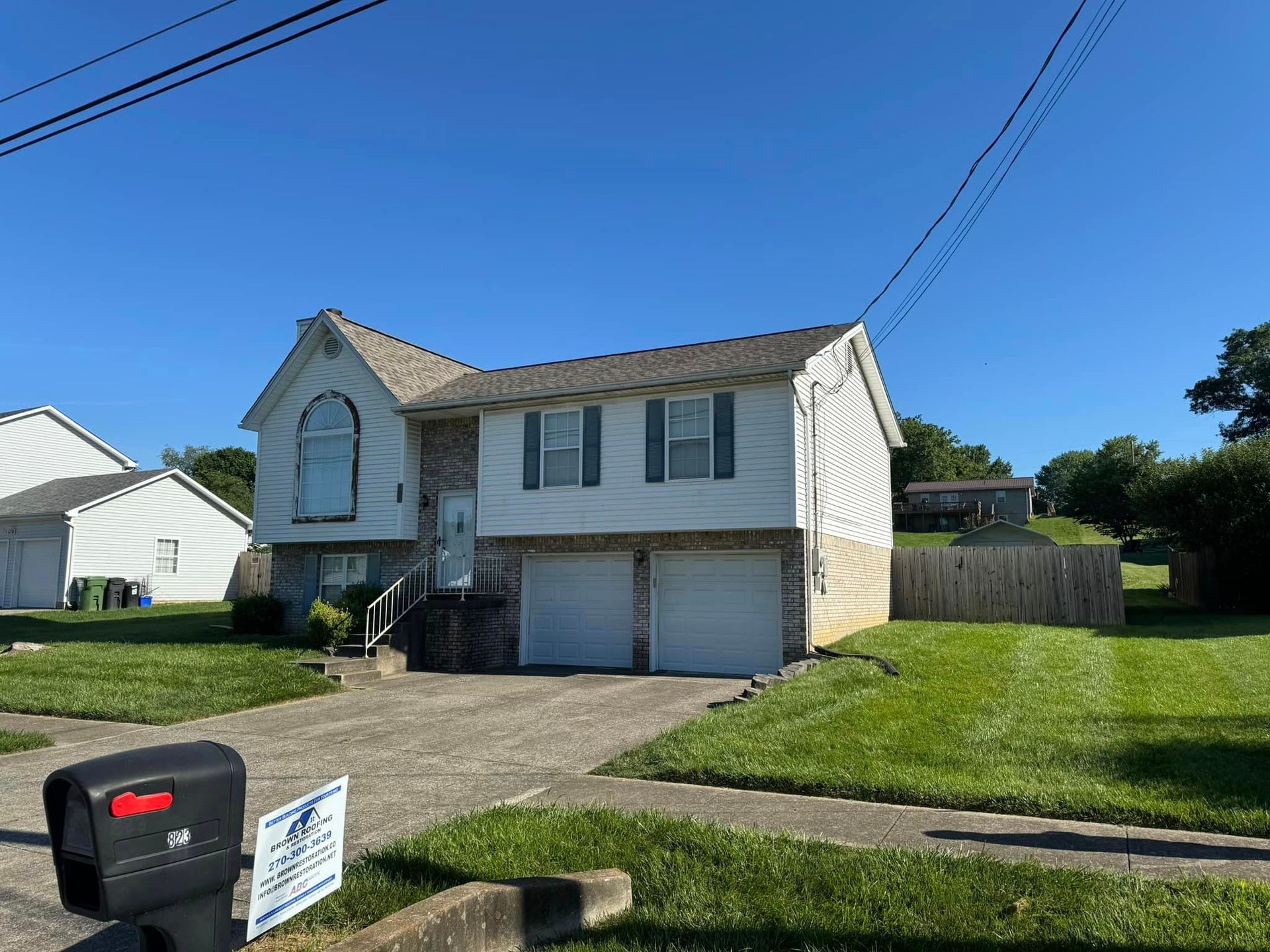 Split-level house with two-car garage, green lawn, blue sky. Black mailbox in foreground.