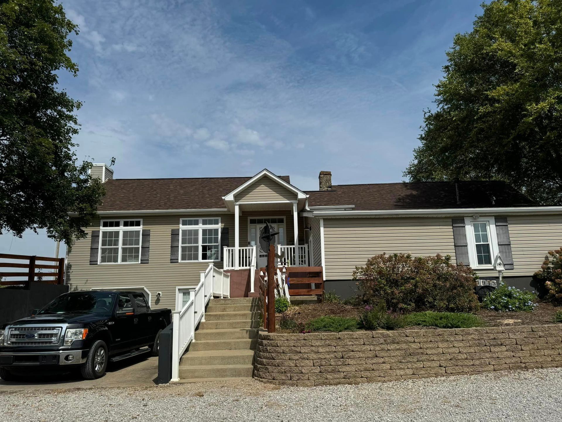 House with a beige exterior, brown roof, and dark truck parked in front. Steps lead to the front door.