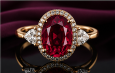 Red oval gemstone ring with diamond accents on a dark reflective background