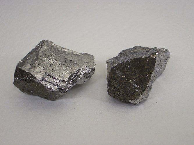 Two irregularly shaped, gray-colored silicon chunks on a light surface.