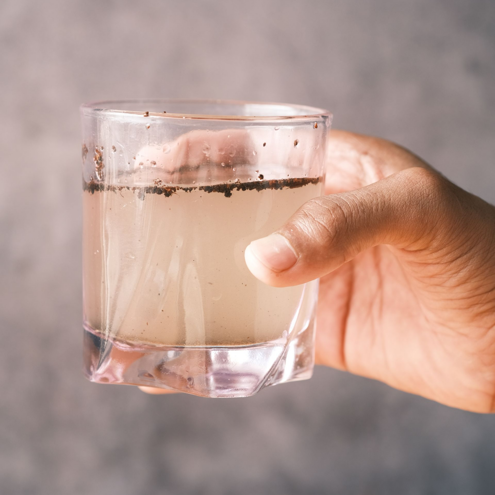 Hand holding a glass of cloudy, brown liquid; flecks floating in it.