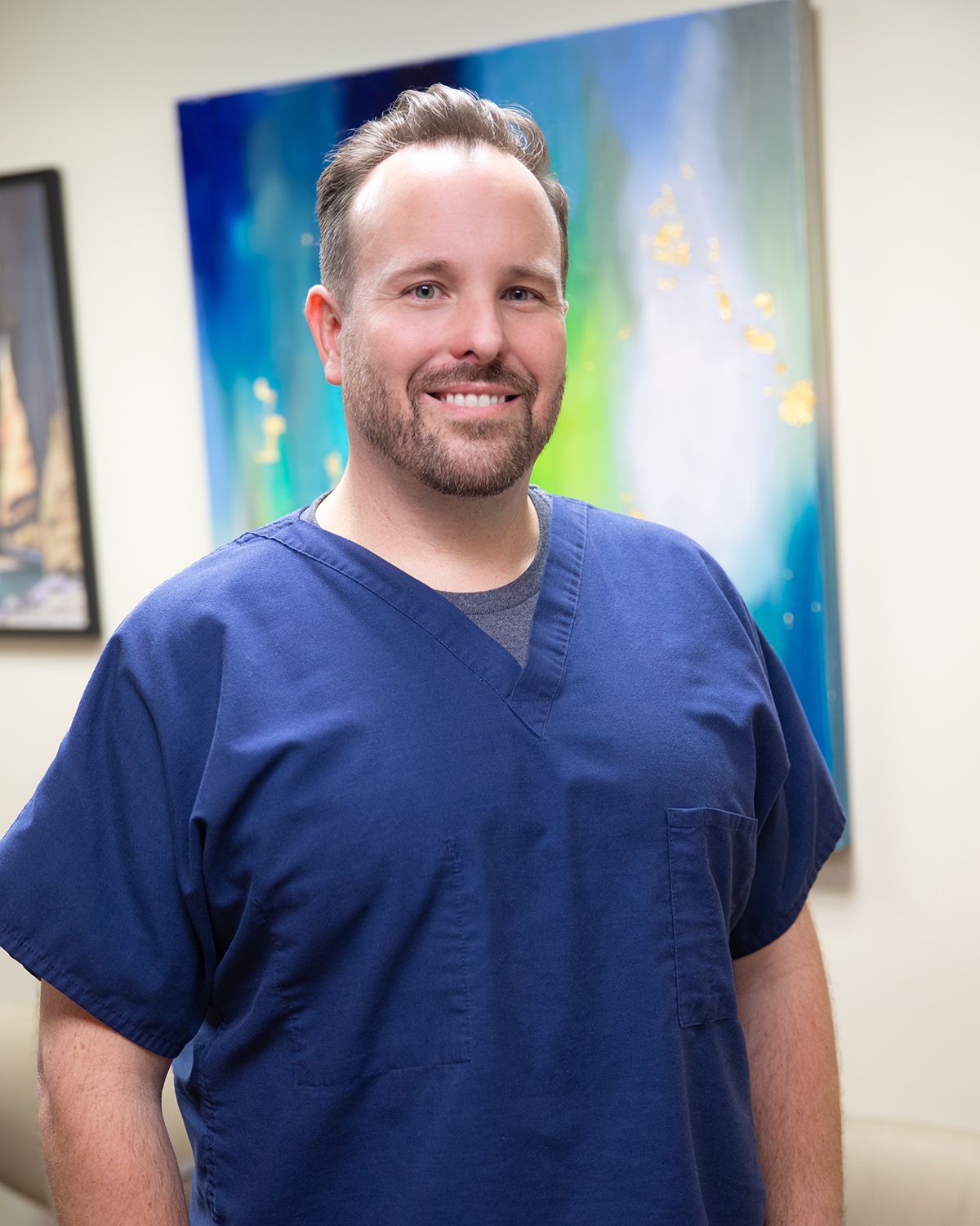 A man in a blue scrub is standing in front of a painting.