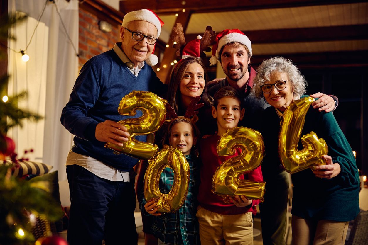 Group celebrating New Year indoors, smiling and holding gold 2026 balloons.