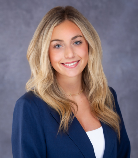 Portrait of a smiling woman in a blue blazer over a white top against a gray backdrop
