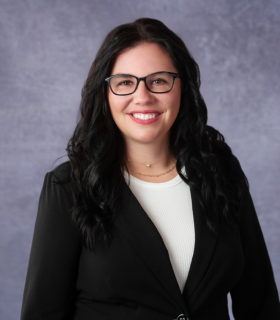Smiling professional in glasses and black blazer against a gray studio backdrop