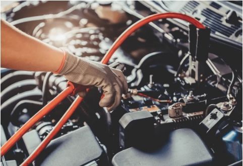 Gloved hand working on engine wiring with red hoses in a car repair shop