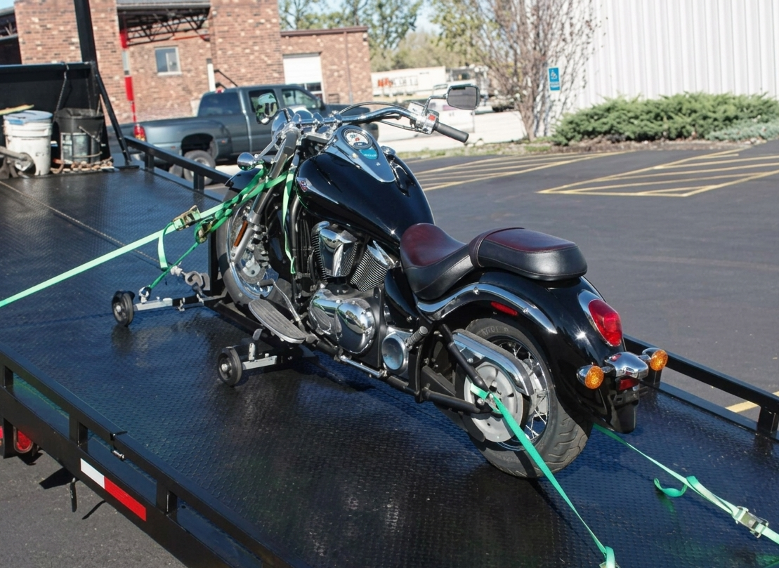 Black motorcycle strapped on a flatbed trailer in a parking lot