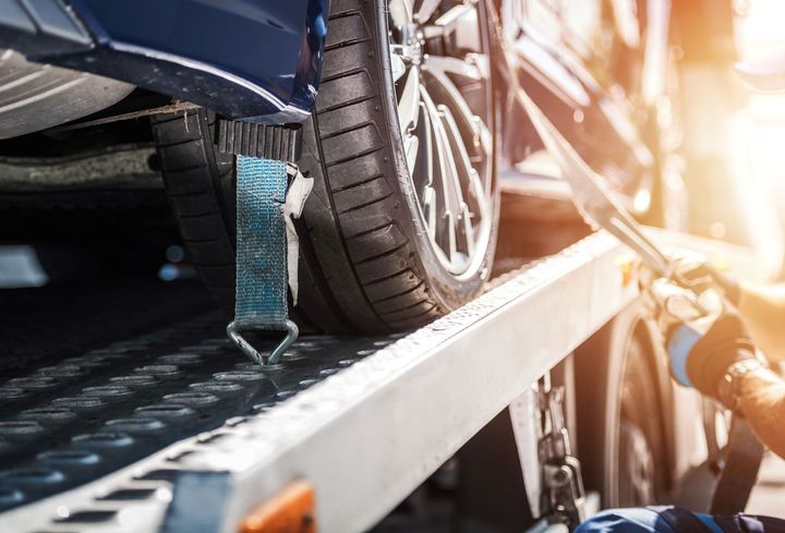 Car wheel strapped to a tow truck ramp in bright sunlight