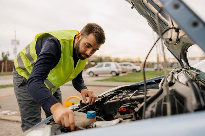 Mechanic in a neon vest checks a car engine on a roadside during a breakdown