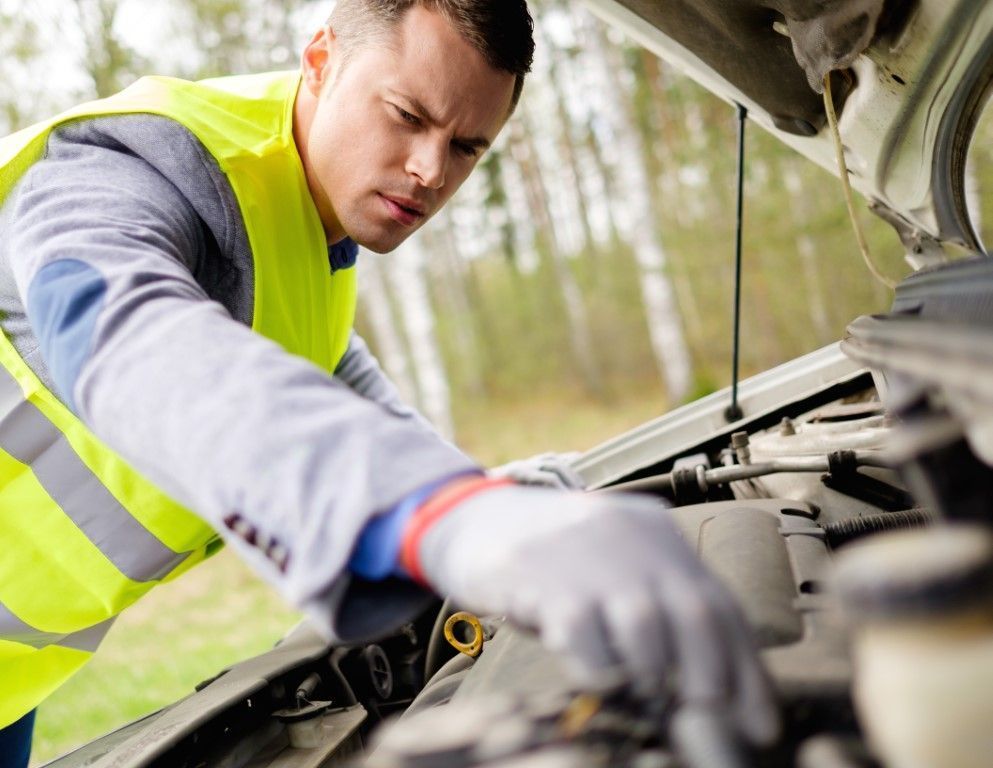 Mechanic in a neon safety vest working under an open car hood outdoors