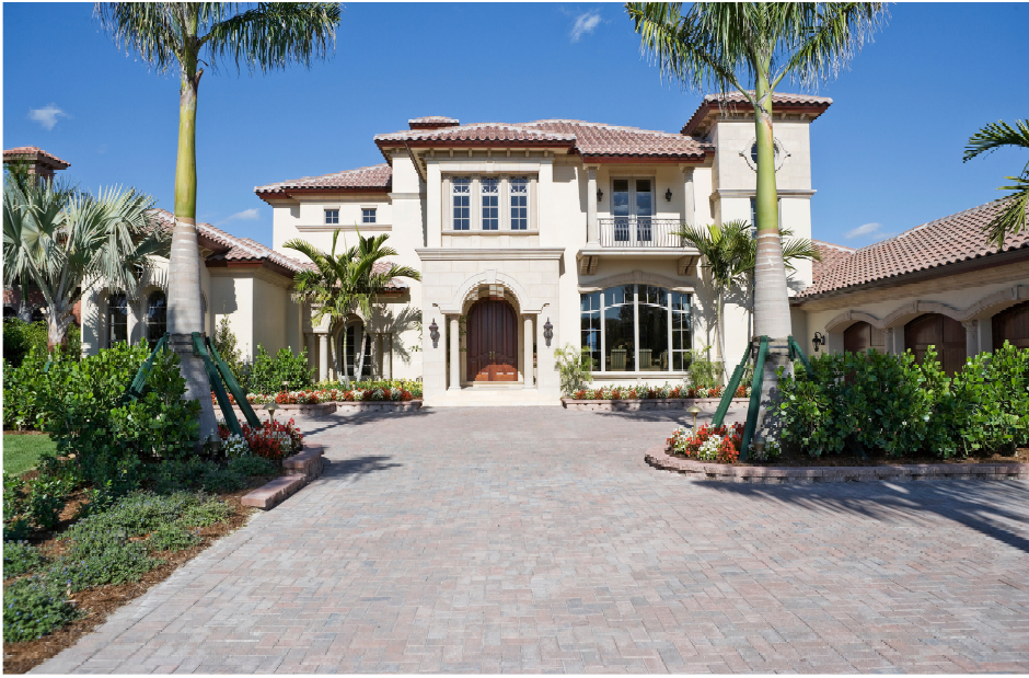 Lord of homes with brick, long driveway, clear skies, palm trees, and green grass.