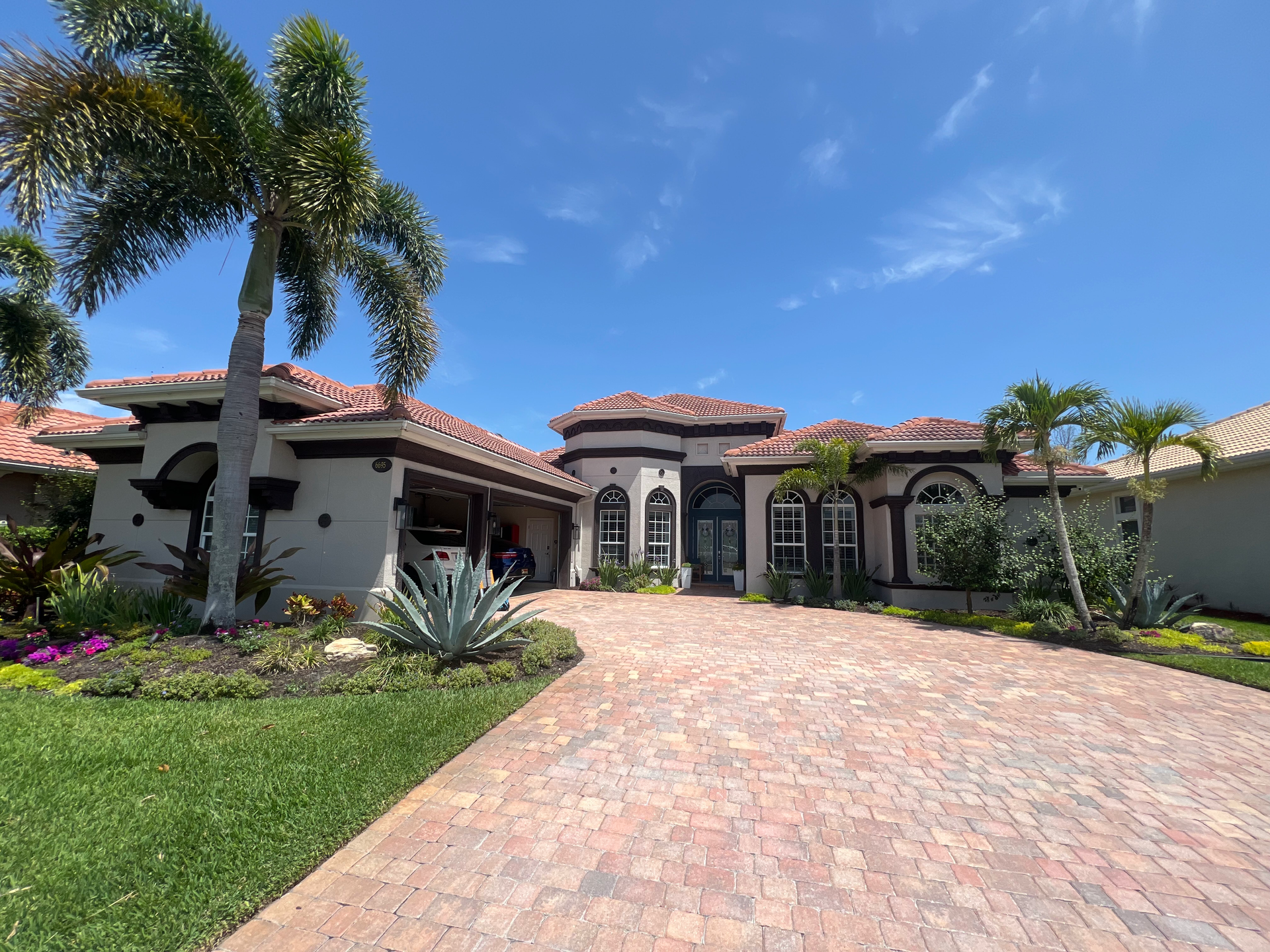 Florida home with red roof, white walls and brown detailing around windows. Long brick driveway.