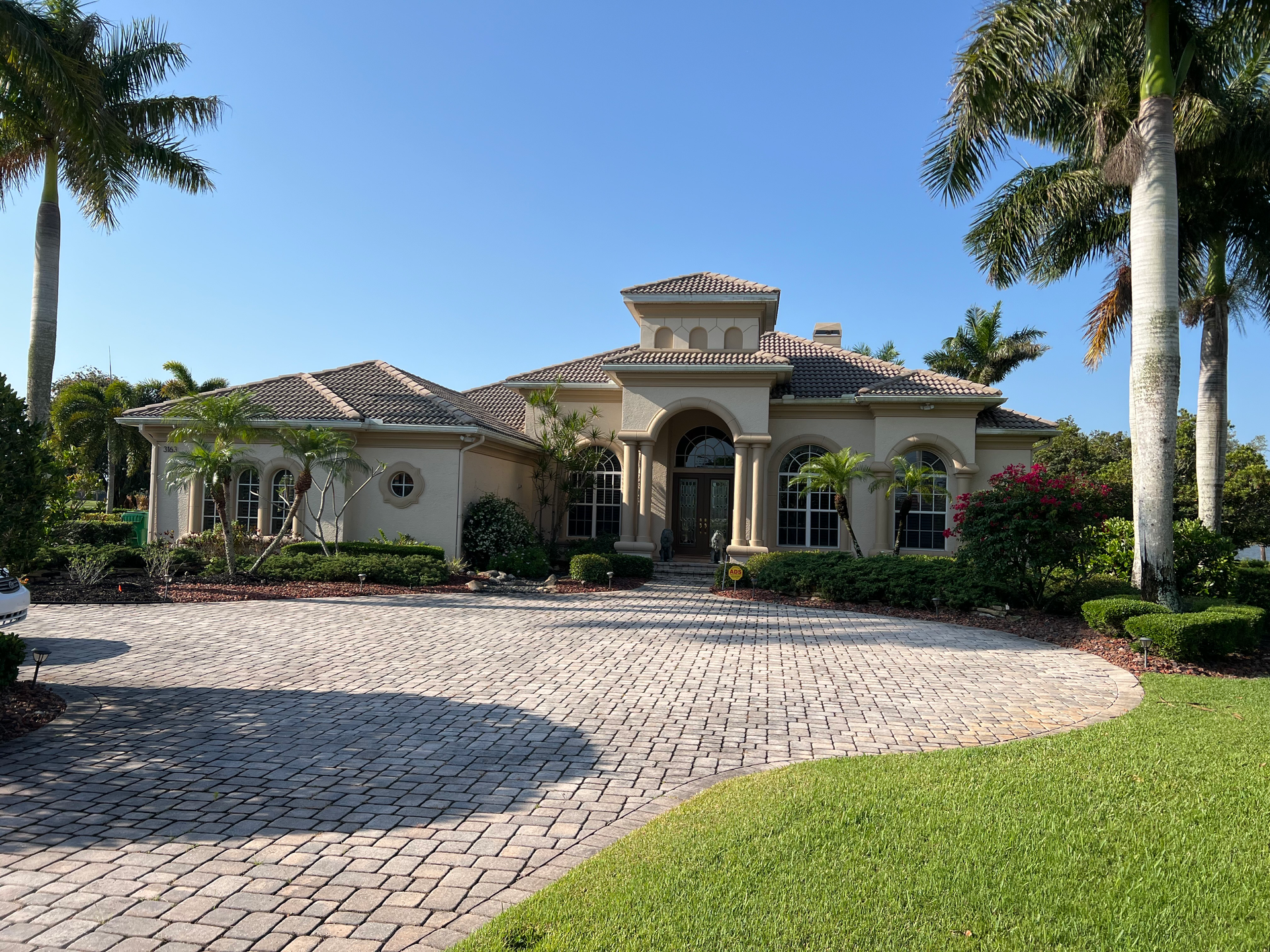 Beige home with a brick long driveway, blue clear sky.