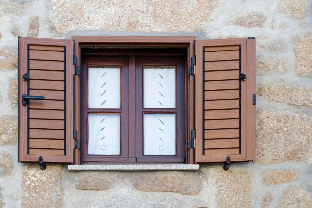 Finestra con persiane in legno aperte contro un muro di pietra.