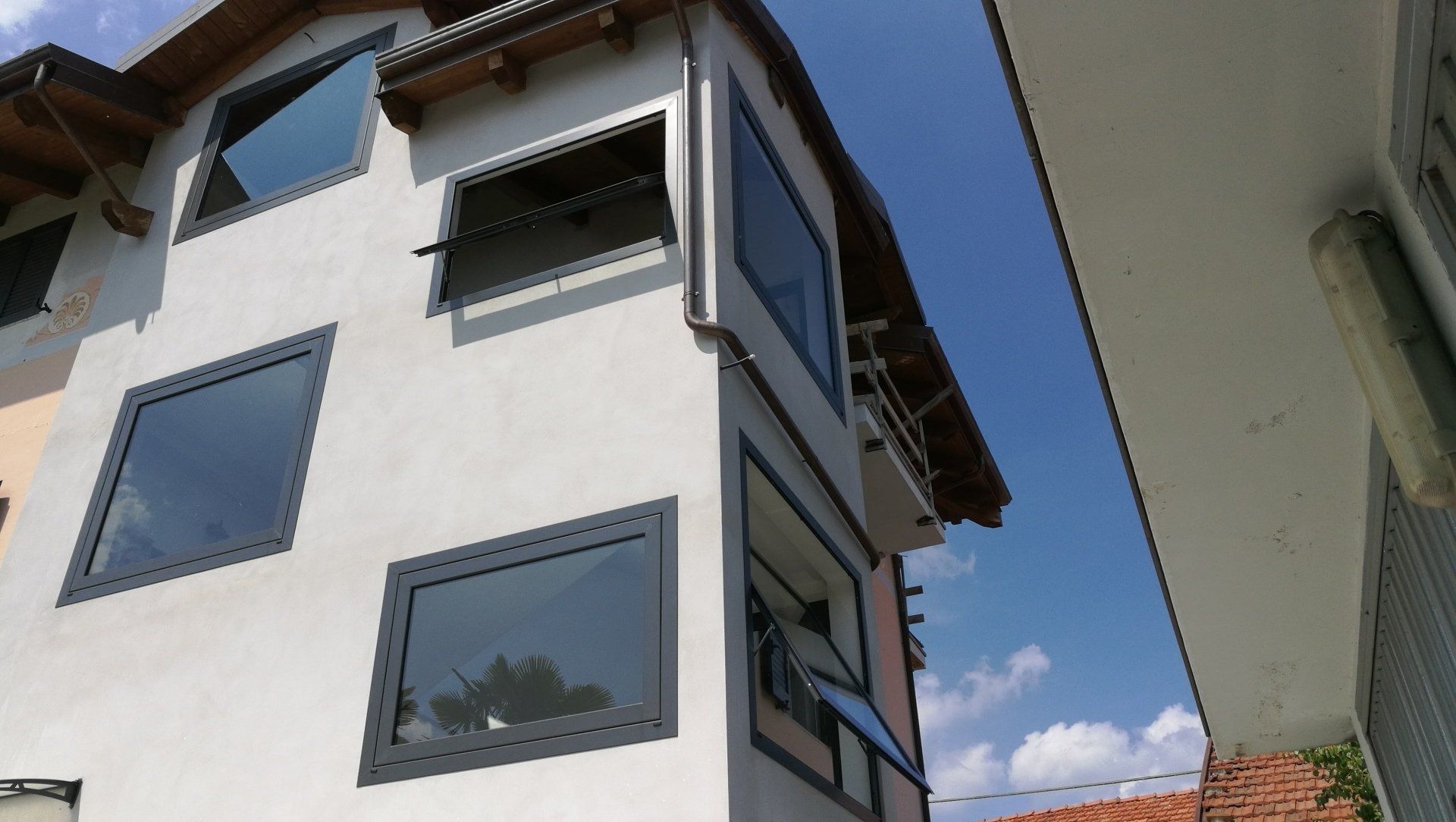 Edificio bianco con finestre con cornici grigie che si stagliano contro il cielo azzurro. Alcune finestre sono aperte.