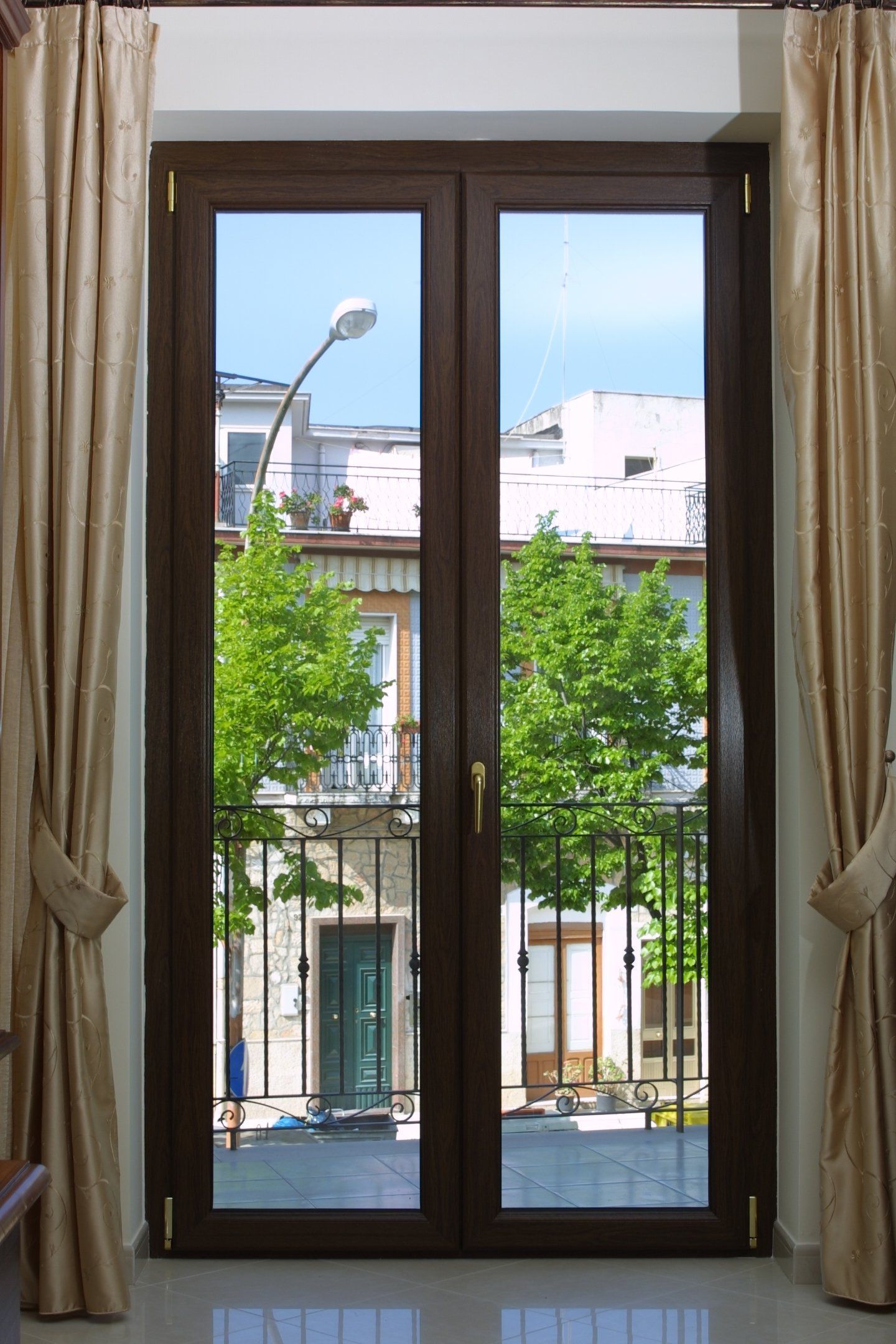 Finestra con cornice marrone e vista sulla strada, sugli alberi e sugli edifici. Tende color marrone chiaro incorniciano la finestra.