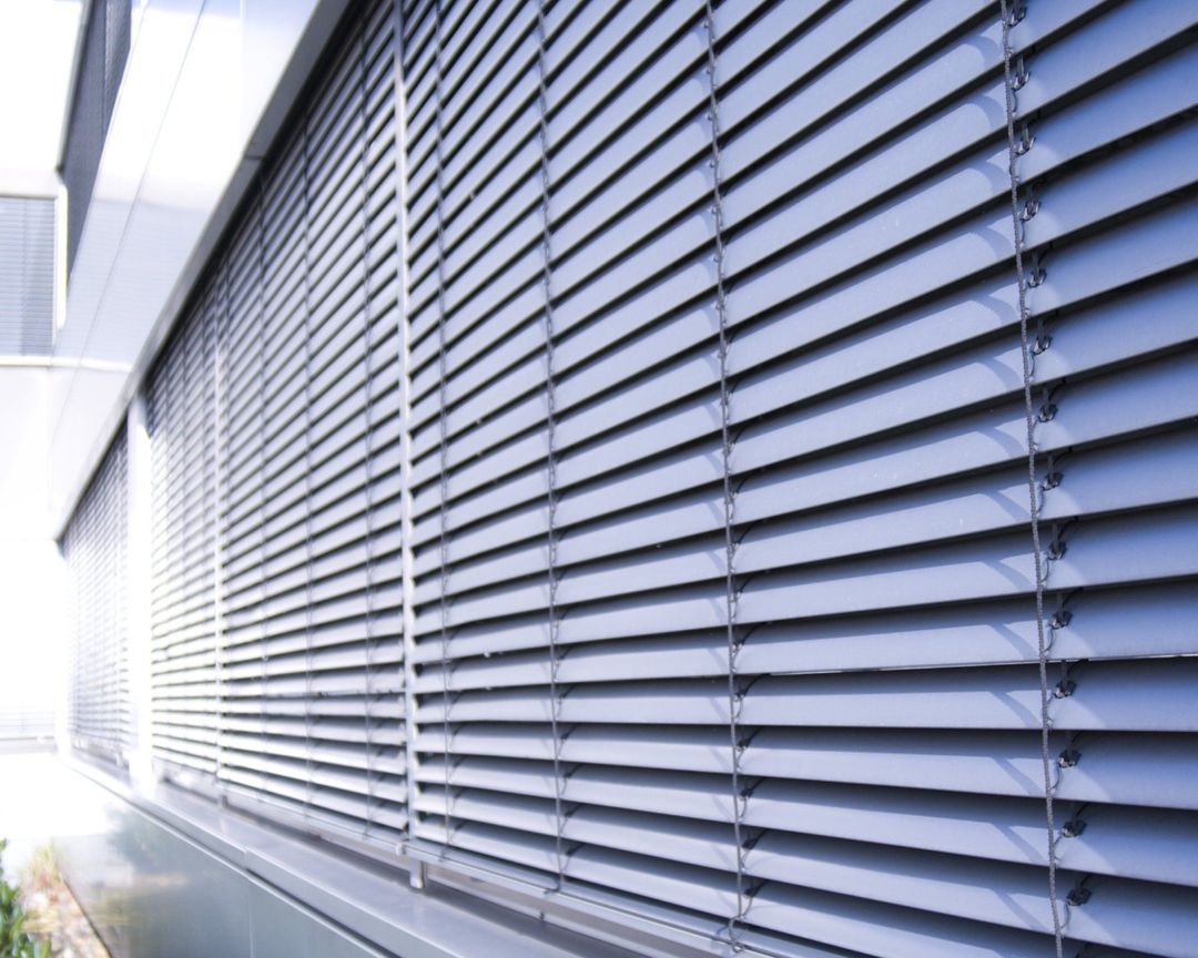 Tende orizzontali grigie sulla facciata esterna di un edificio, angolate per controllare la luce.