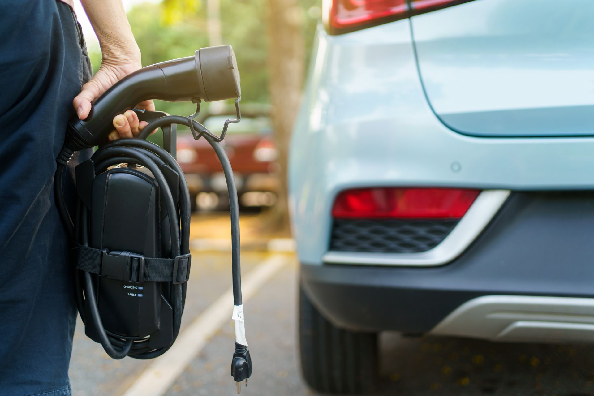 A person is holding a charging cable in front of an electric car.
