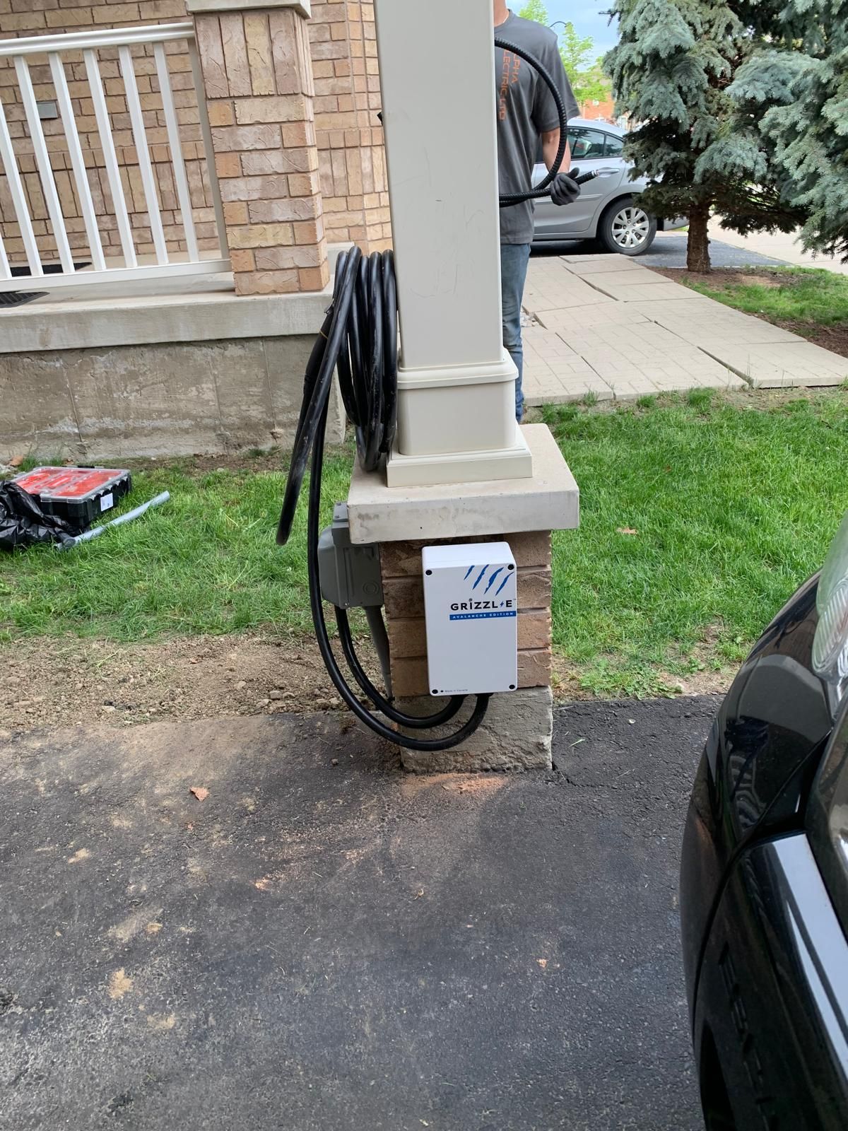 A car is parked in front of a house with an ev charging port on a post