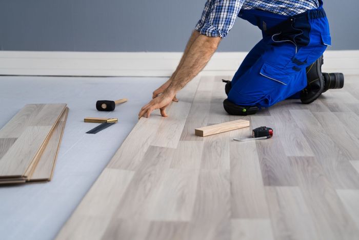 A person kneeling and installing laminate flooring