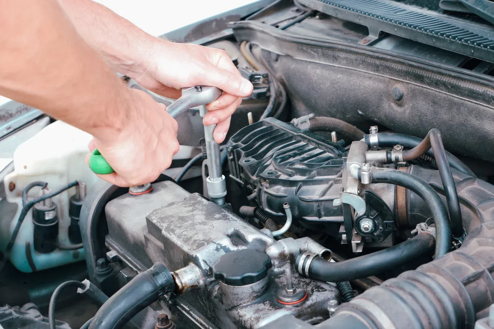 A person is working on a car engine with a wrench.