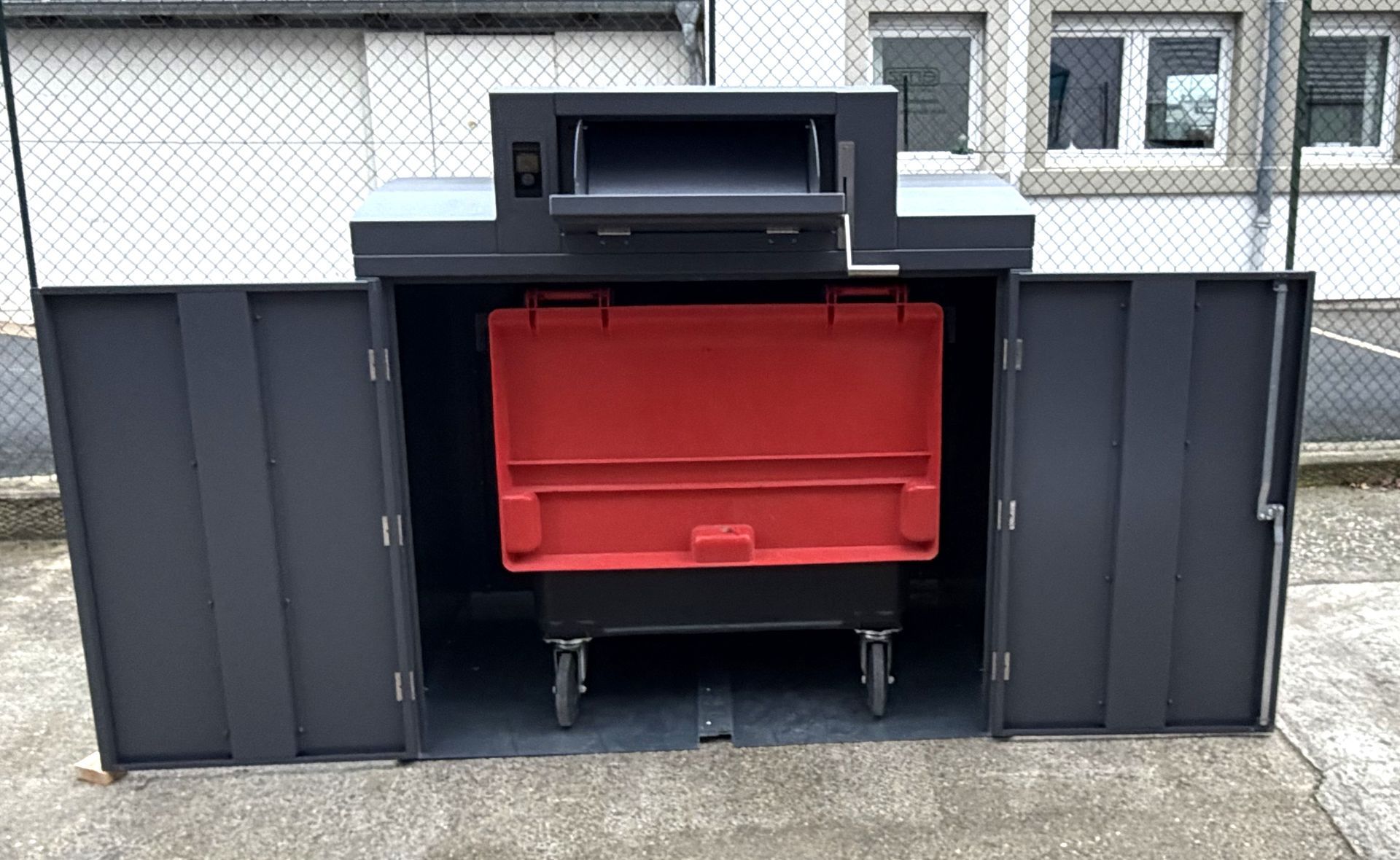 Un conteneur à déchets gris foncé, portes ouvertes laissant apparaître une poubelle rouge à l'intérieur.