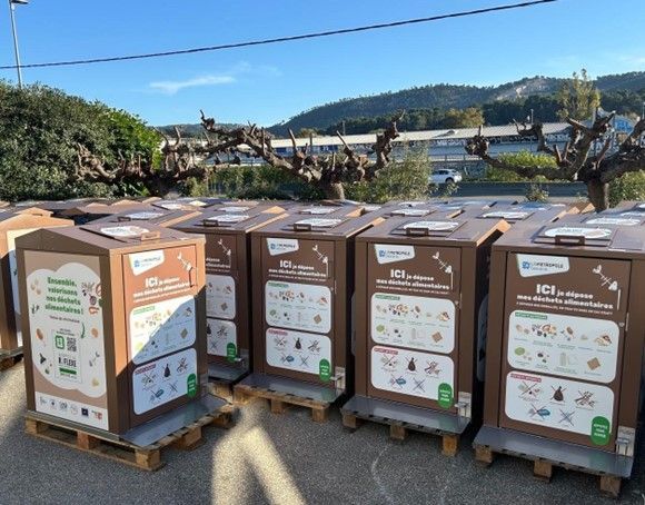 Rangée de bacs de recyclage bruns sur palettes, avec instructions et illustrations, à l'extérieur.