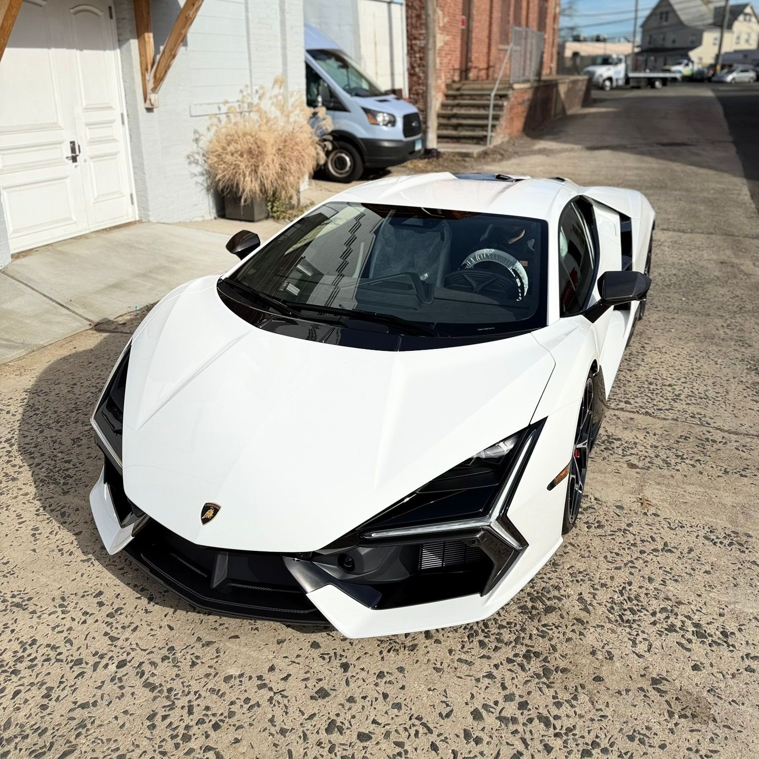 White Lamborghini sports car parked on a cobblestone street, in front of a building.