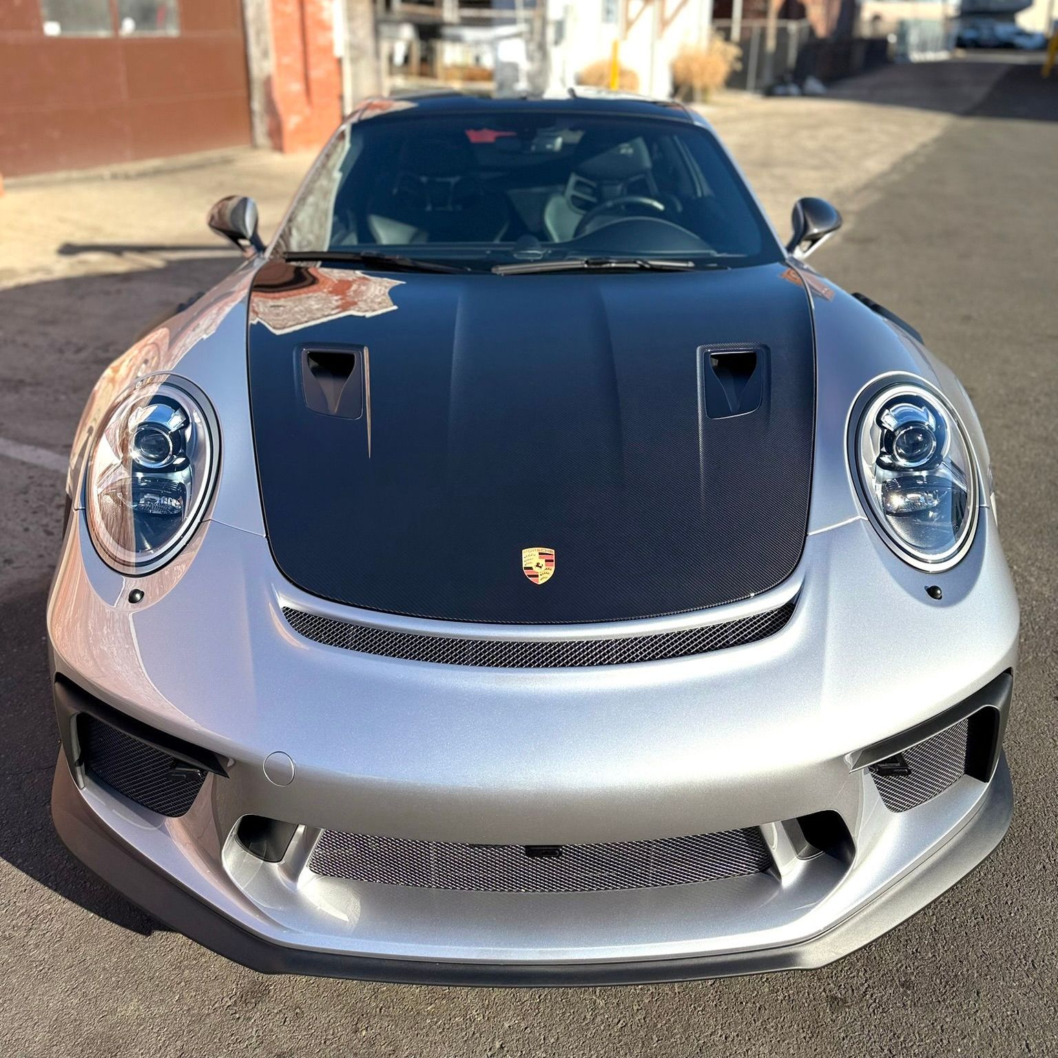Silver Porsche 911 sports car with black hood; parked on asphalt in daylight.