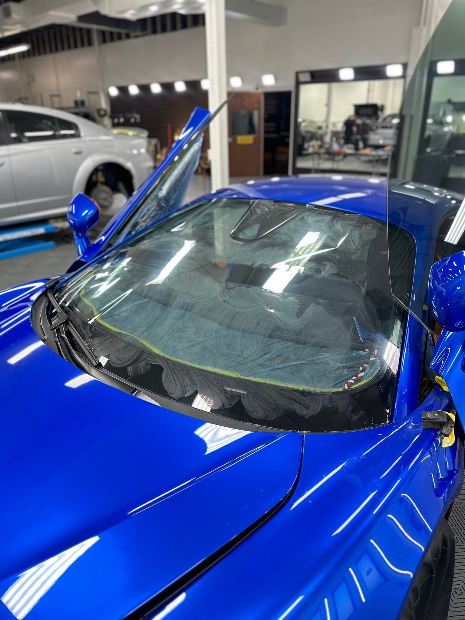 Blue car with tinted windshield, inside a detailing shop.