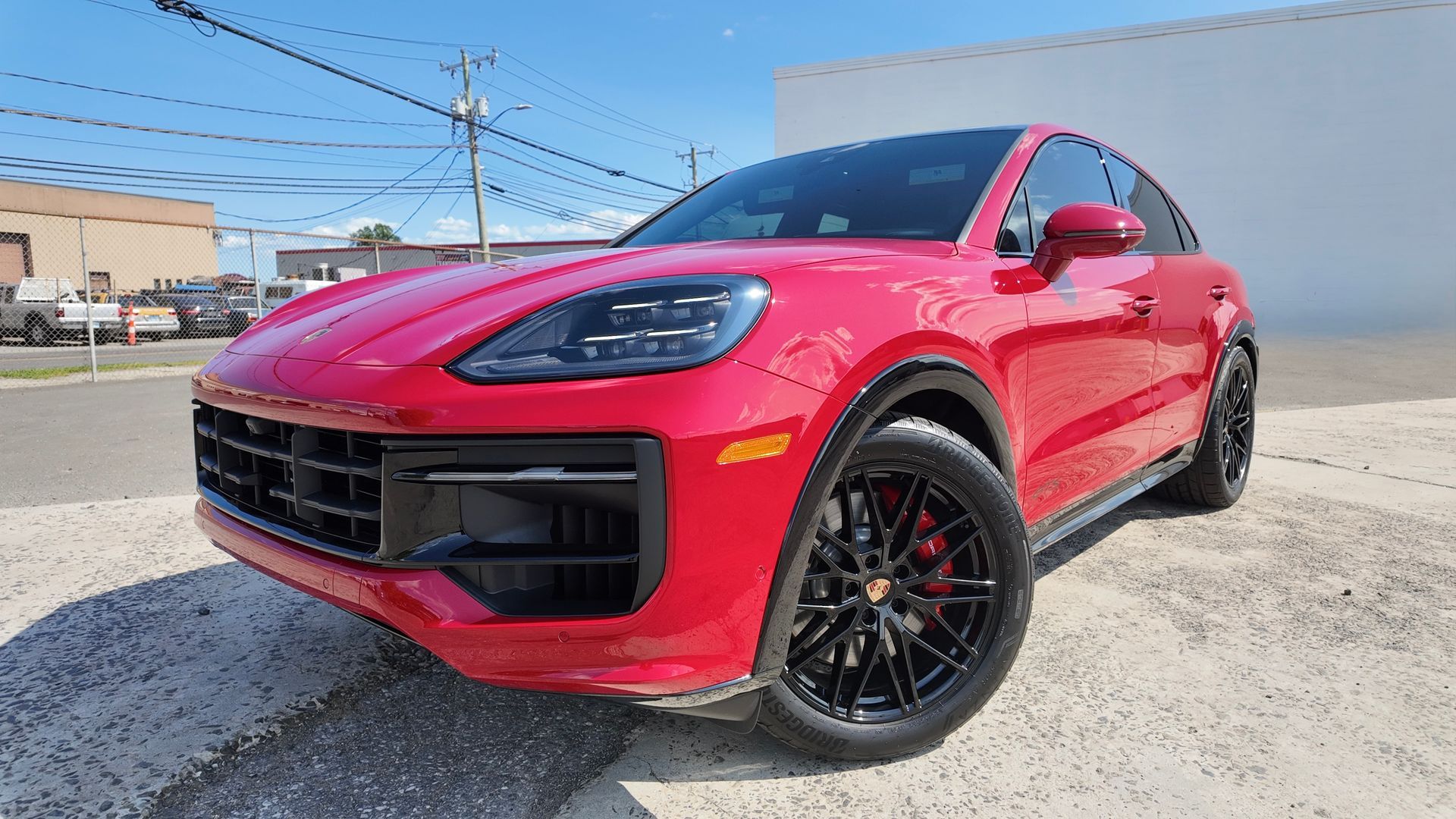 Red Porsche SUV, black wheels, parked outdoors under a blue sky.