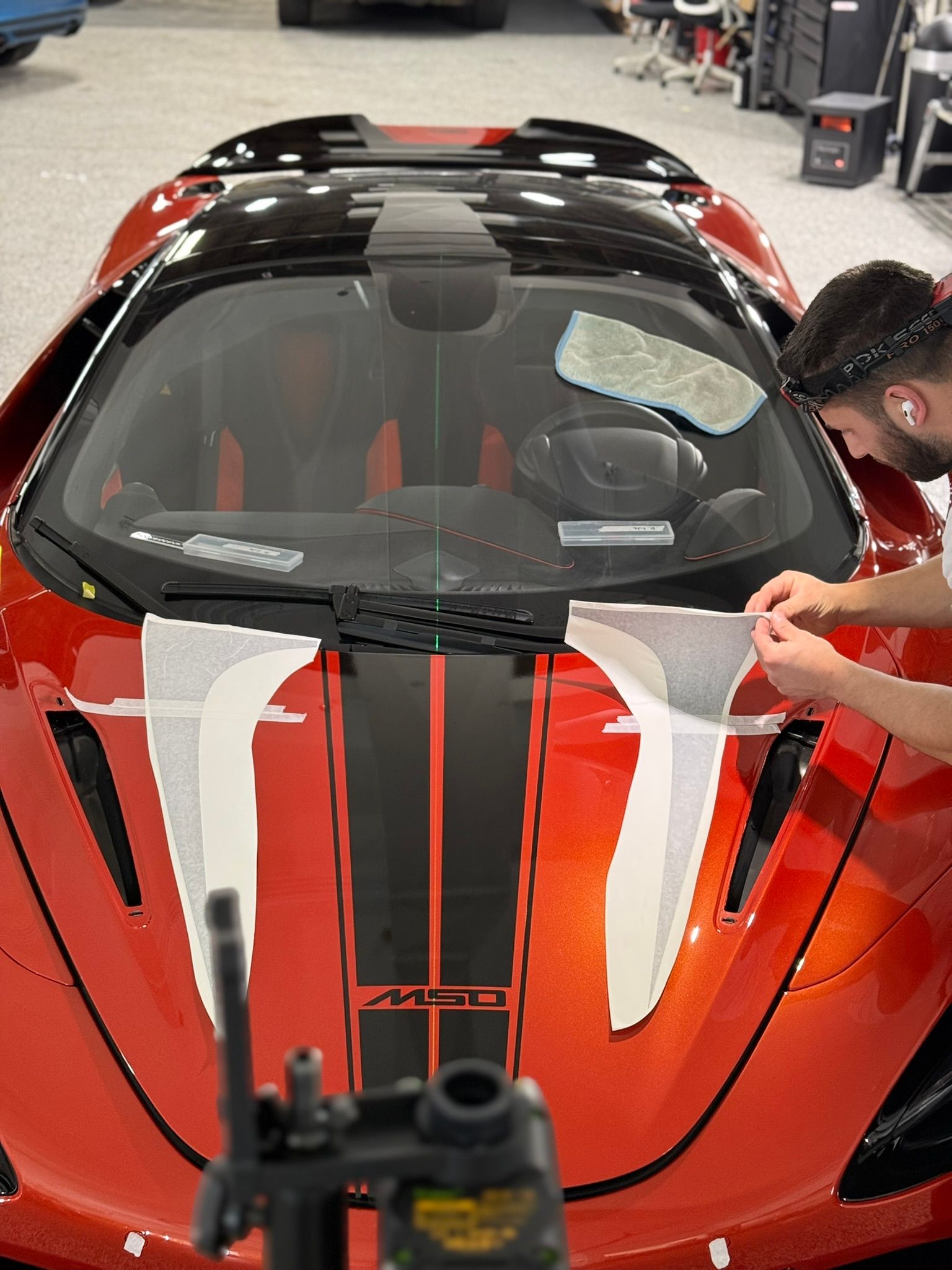 Person applying wrap to a red McLaren with black stripes in a garage.