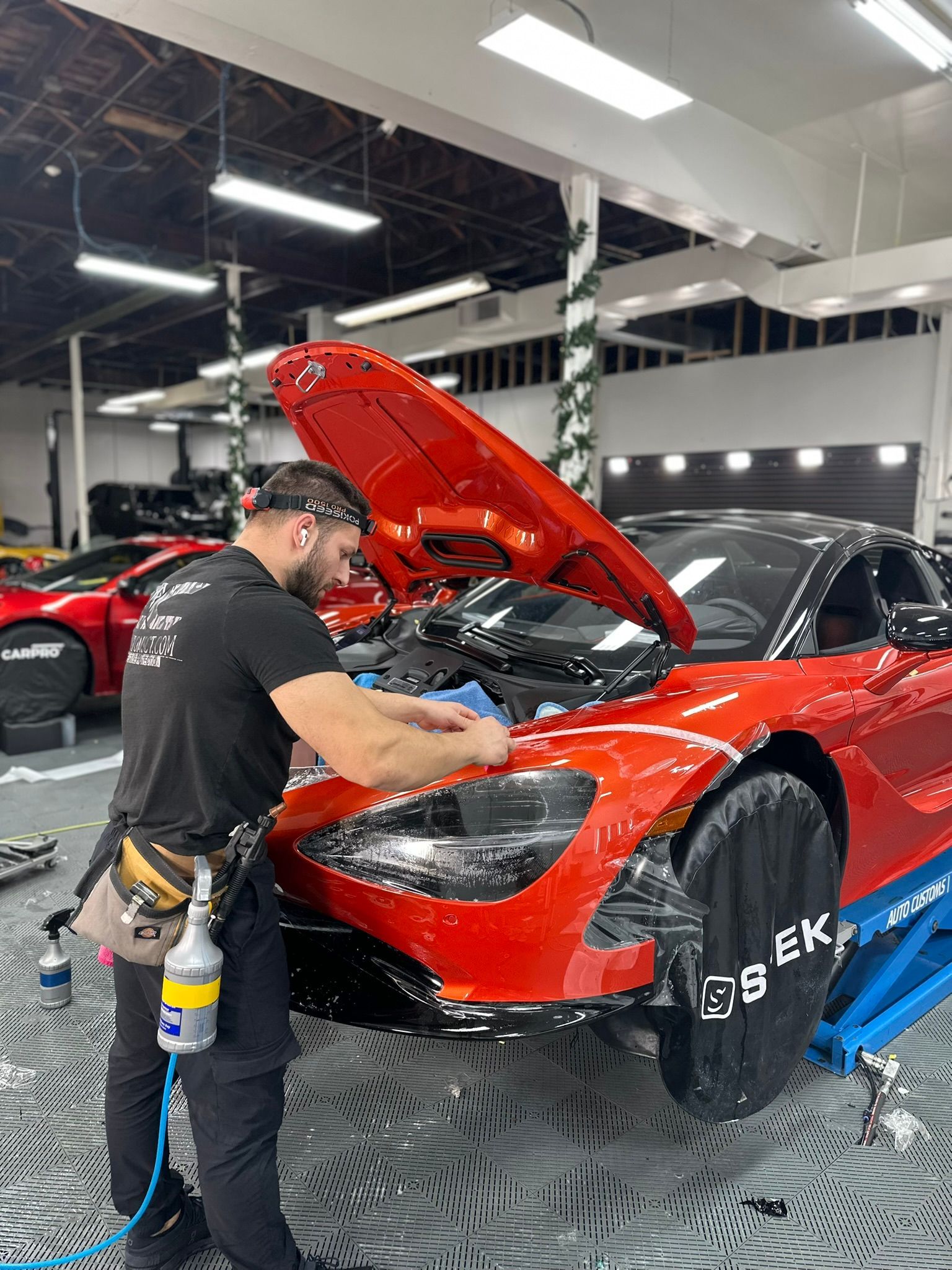 Mechanic applies film to a red sports car. Garage setting.