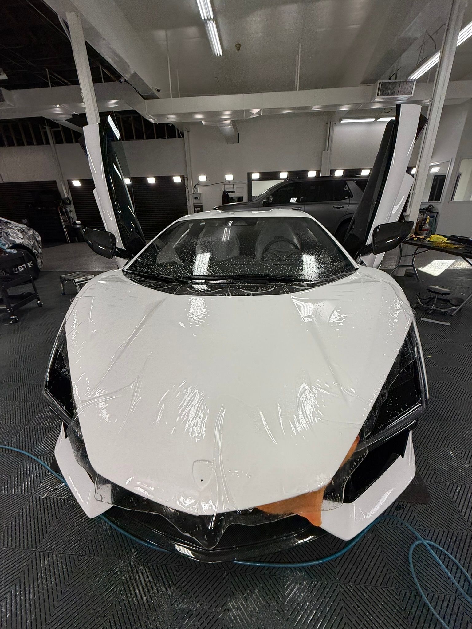 White sports car with open doors being washed in a car wash.