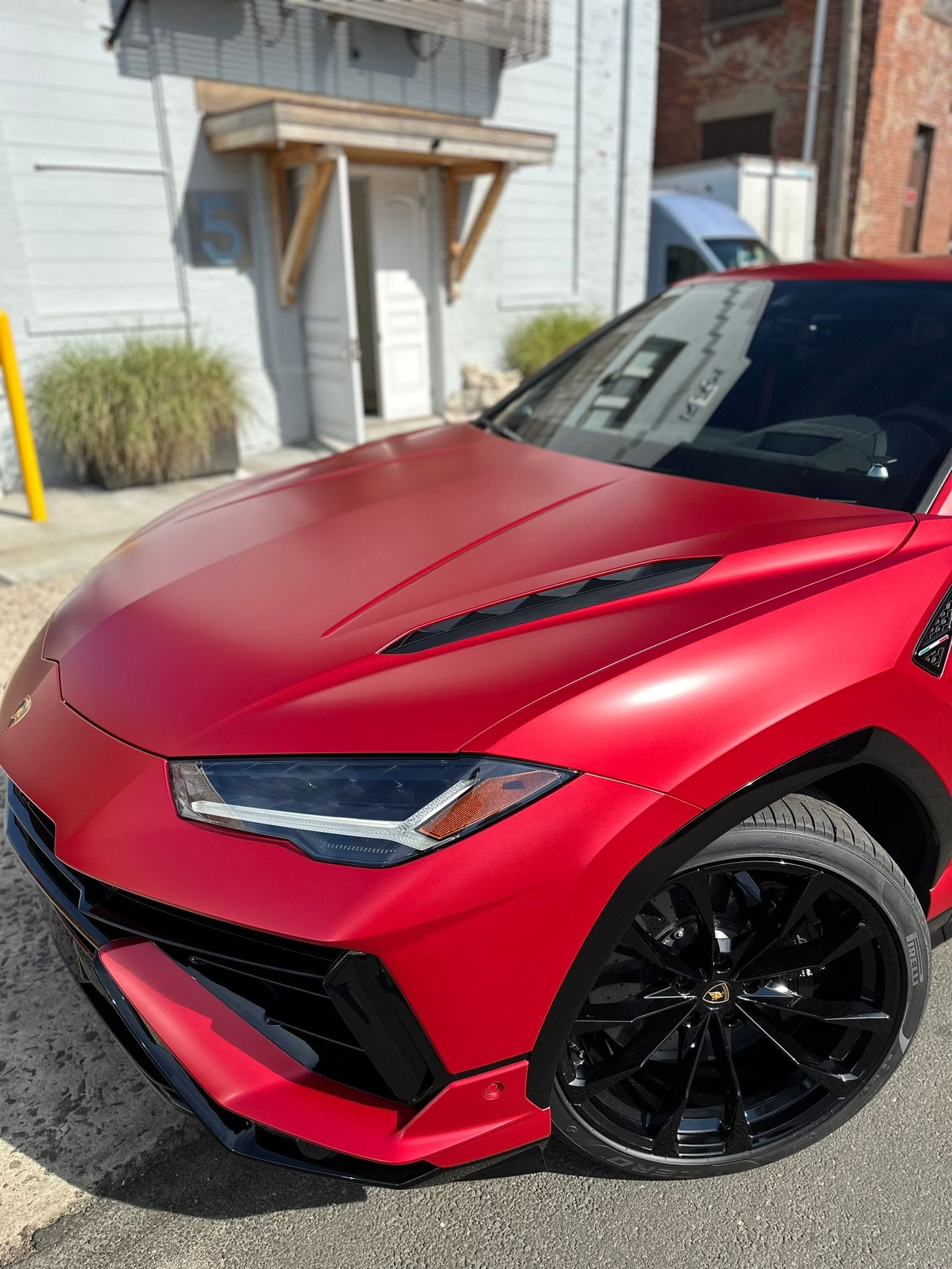 Red Lamborghini Urus SUV with black wheels parked in front of a building.