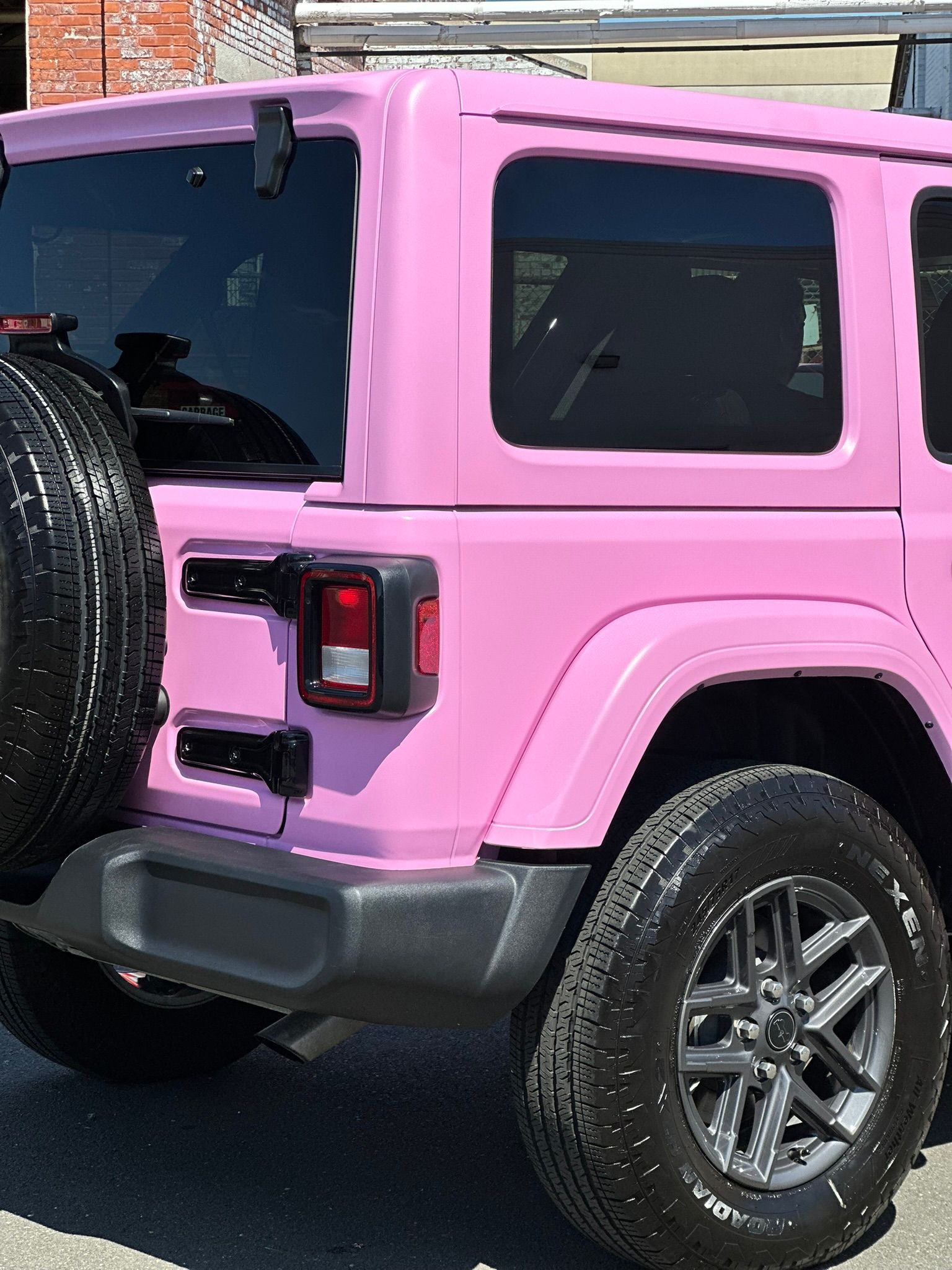 Pink Jeep Wrangler, black tire and trim, on a street.