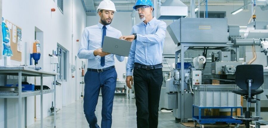 Two men are walking down a hallway in a factory looking at a clipboard.