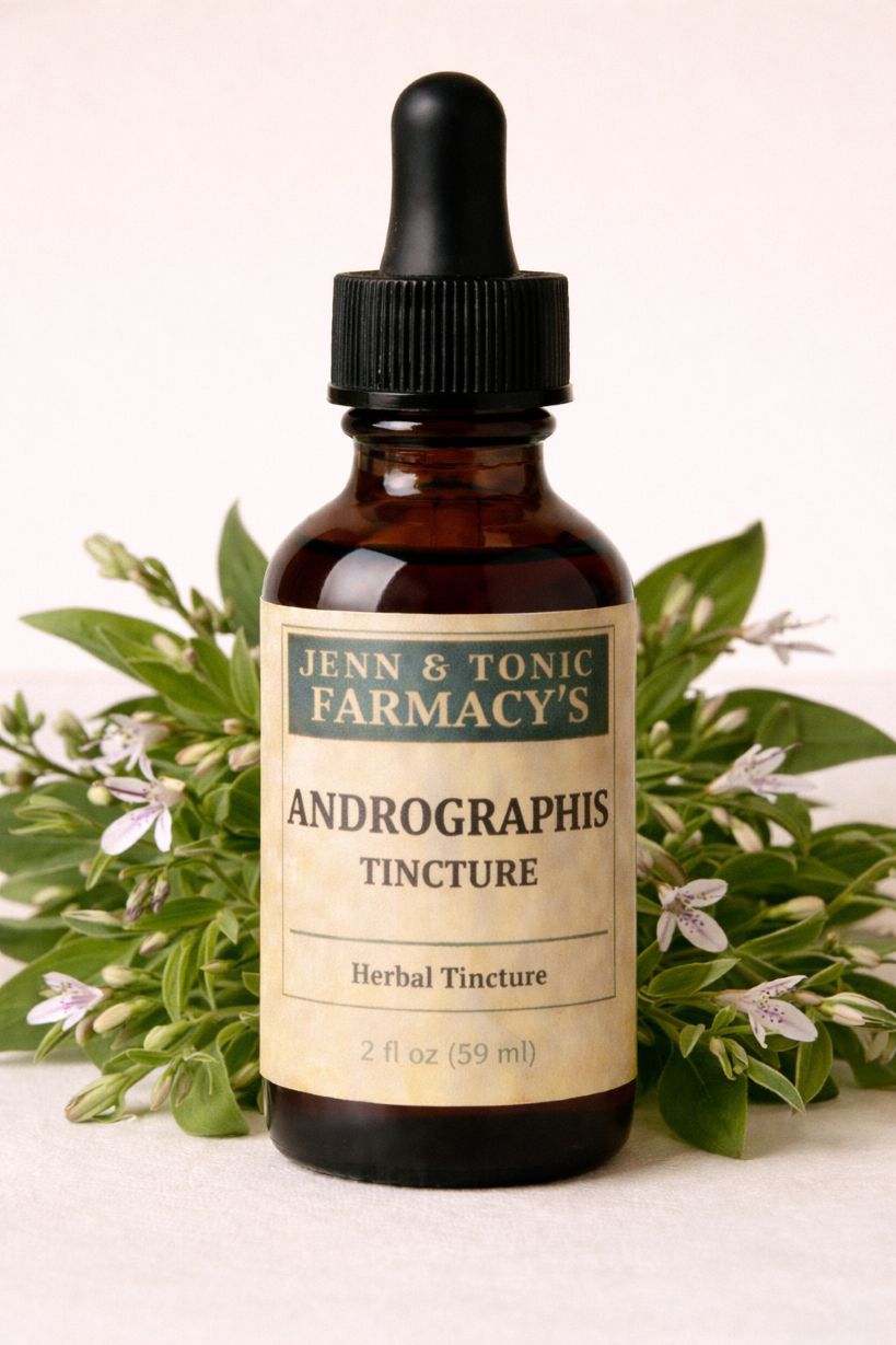 A brown glass dropper bottle of Jenn & Tonic Farmacy’s Andrographis tincture, set against a backdrop of green plant sprigs.