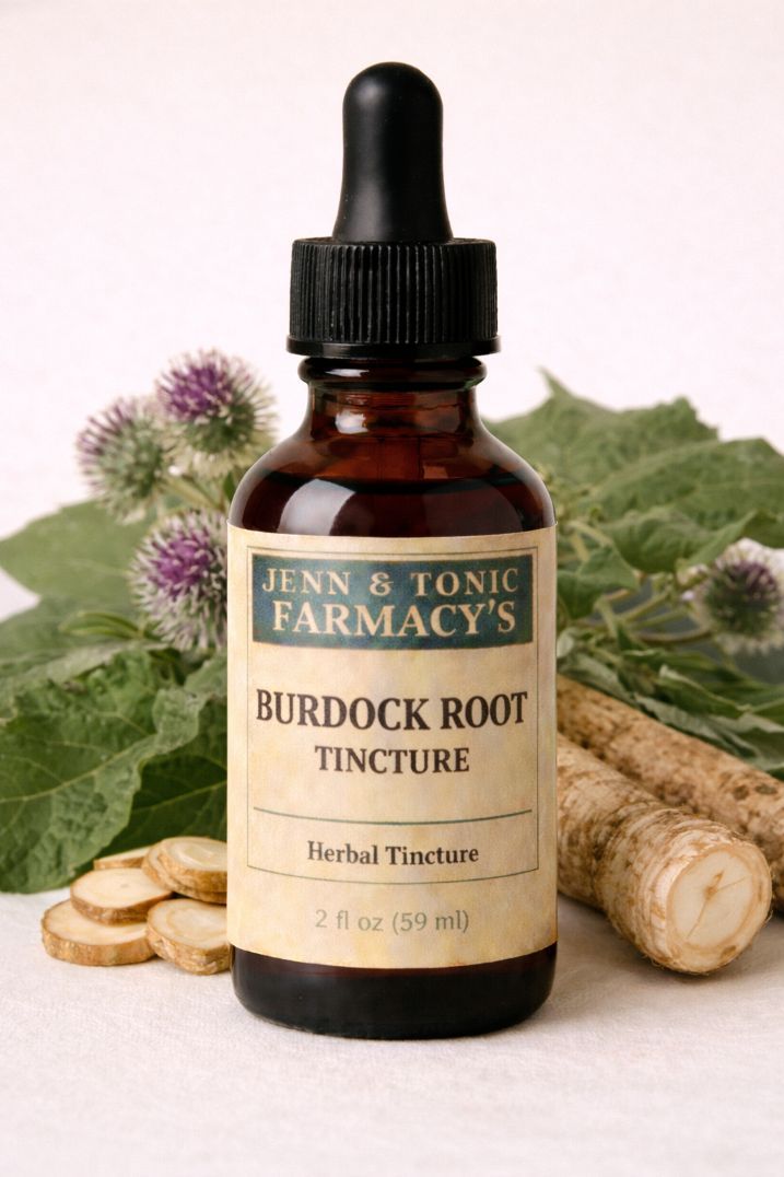 A bottle of Jenn & Tonic Farmacy’s Burdock Root tincture, surrounded by burdock roots, leaves, and purple flowers.